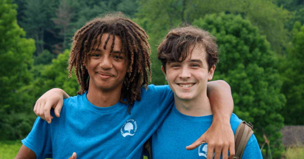 Two young people smiling outdoors in Delaware Nature Society shirts.