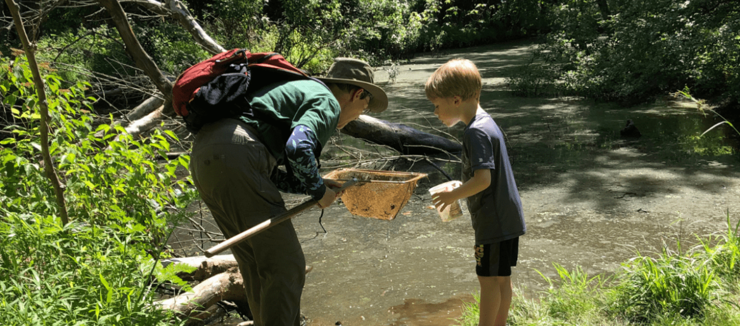 A man and a child using a long-handled net during an outdoor water activity.