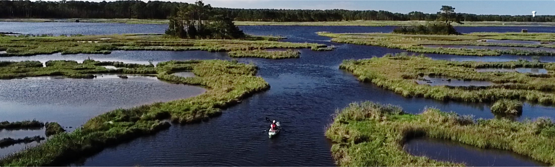 Aerial view of a marshland river with a person paddling a kayak.