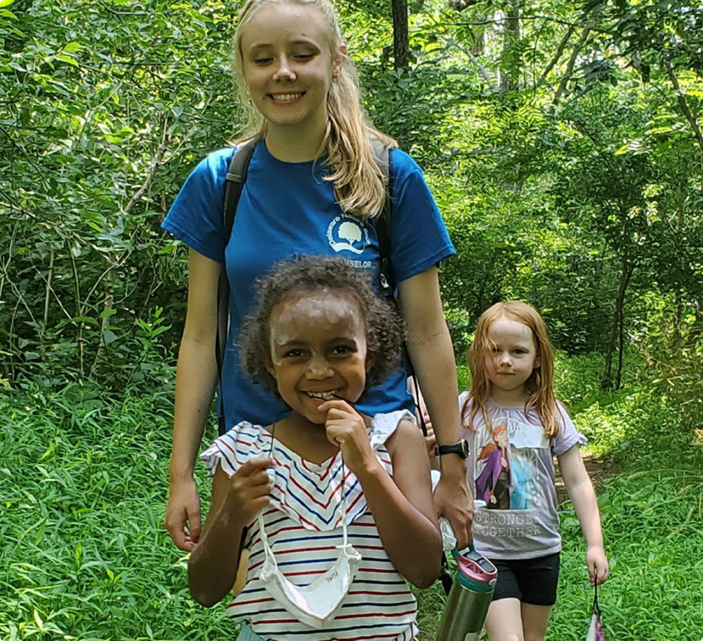 Children and a volunteer walking together on a wooded trail.